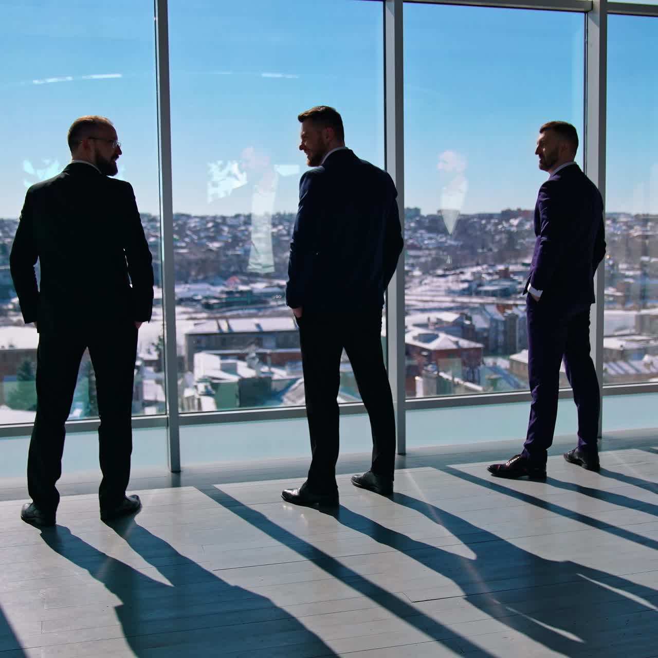 Business partners near windows with city view. Elegant managers in suits having a conversation in the light office room in sunny day. Back view