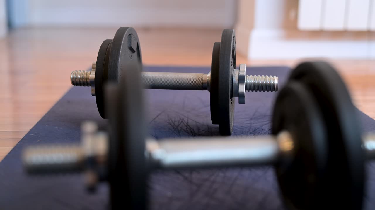 A selective focus close-up on a dumbbell in the background. The fitness equipment lies on an exercise mat, ready for a home workout or strength training session