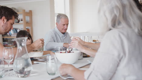 Mehrgenerationenfamilie-Sitzt-Zu-Hause-Am-Tisch-Und-Isst-Gemeinsam