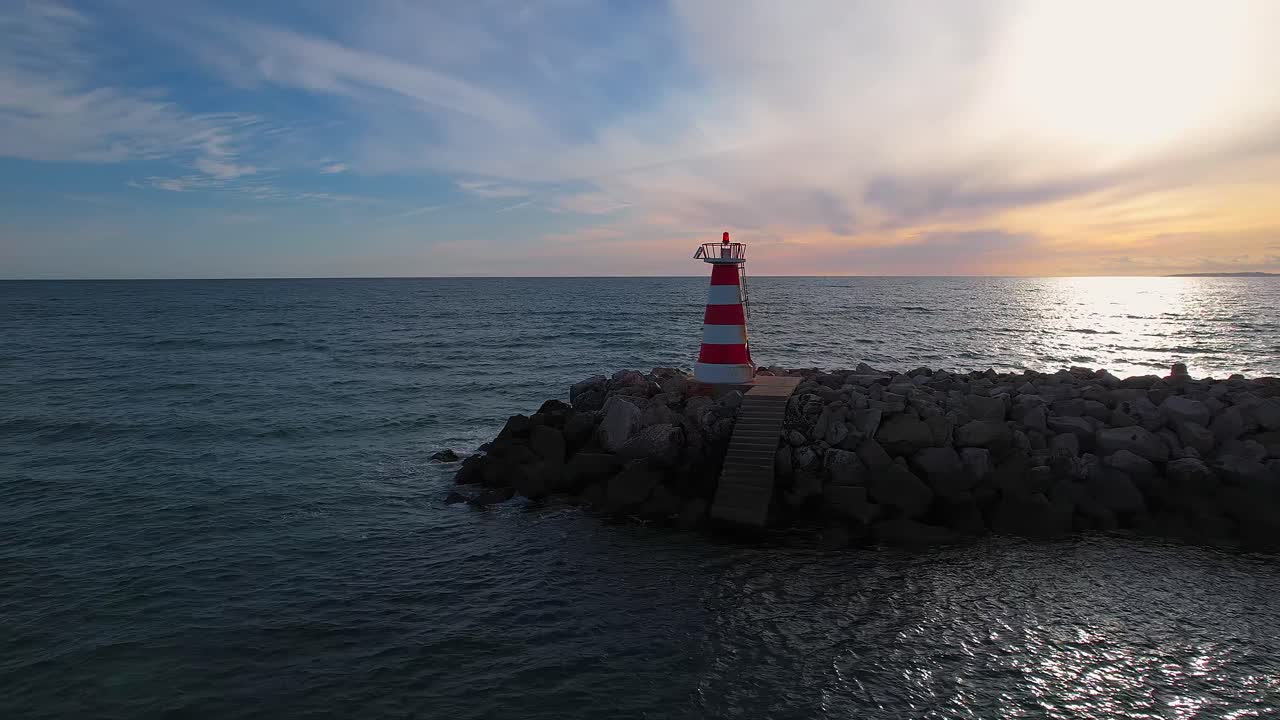 Drone orbit around red and white harbour lighthouse on rocky breakwater at entrance channel to Marina de Vilamoura, next to Vilamoura Beach in Quarteira, Loulé, Faro district, Algarve, Portugal