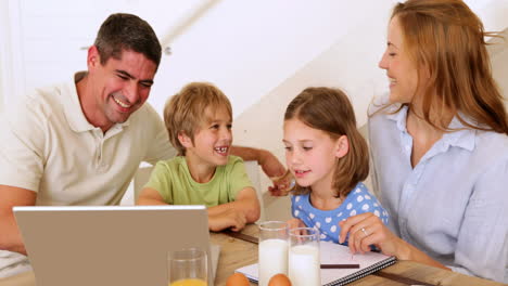 Familia-Feliz-Usando-Una-Computadora-Portátil-Juntos-En-La-Mesa-Del-Desayuno