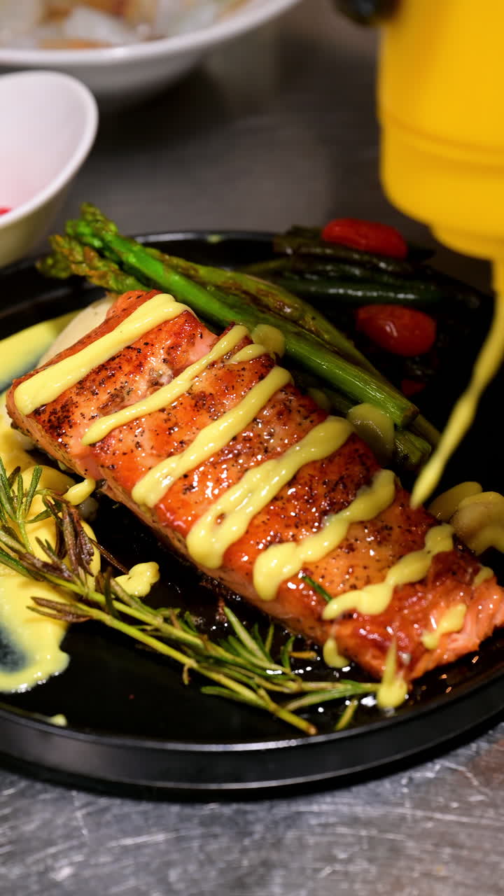 Filetto di salmone grigliato con asparagi e rosmarino su piatto nero. Primo piano di salmone arrosto servito con asparagi, rosmarino e salsa su un piatto gourmet
