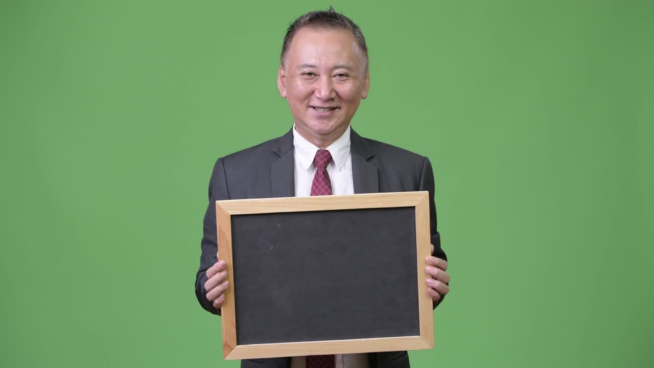 성숙 한 일본인 사업가 가 초록색 배경 에 검은판 을 들고 있다