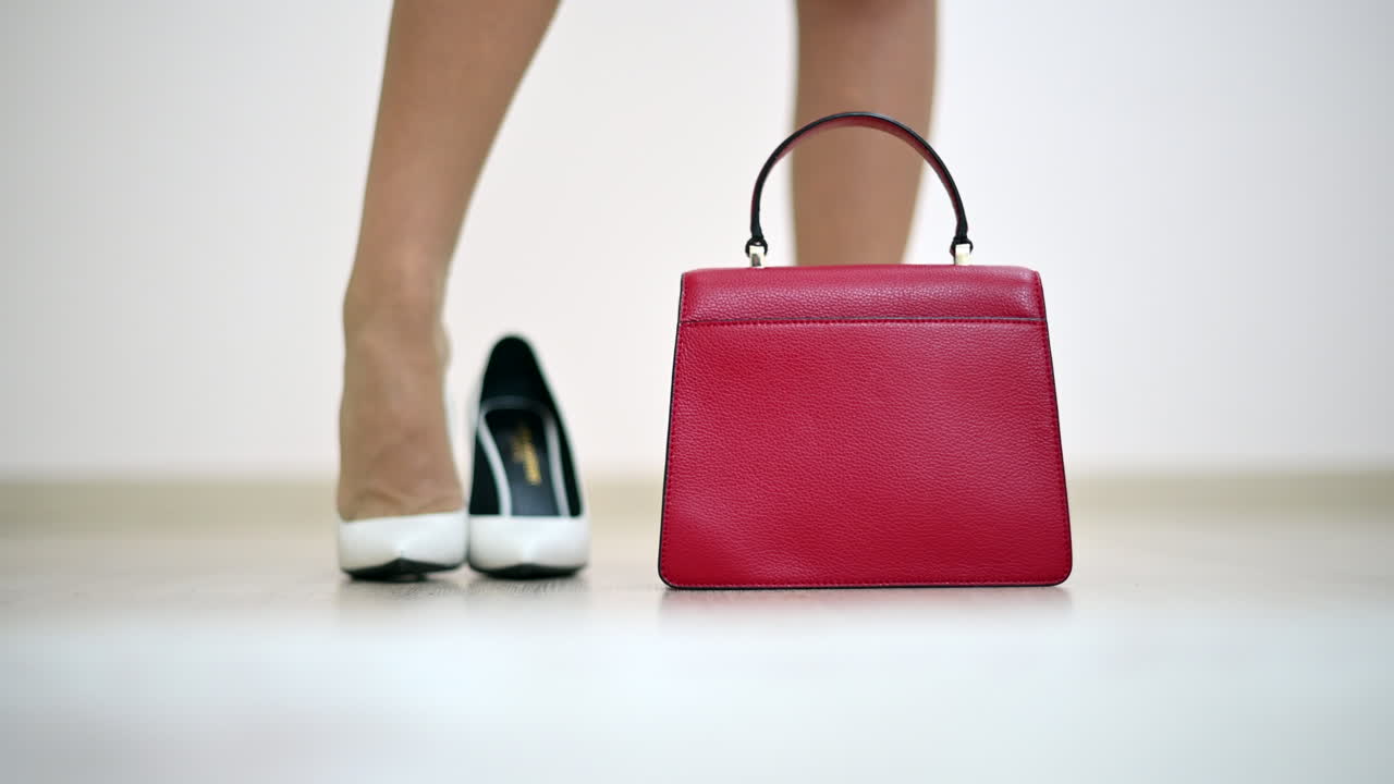 Woman putting on white shoes and red purse