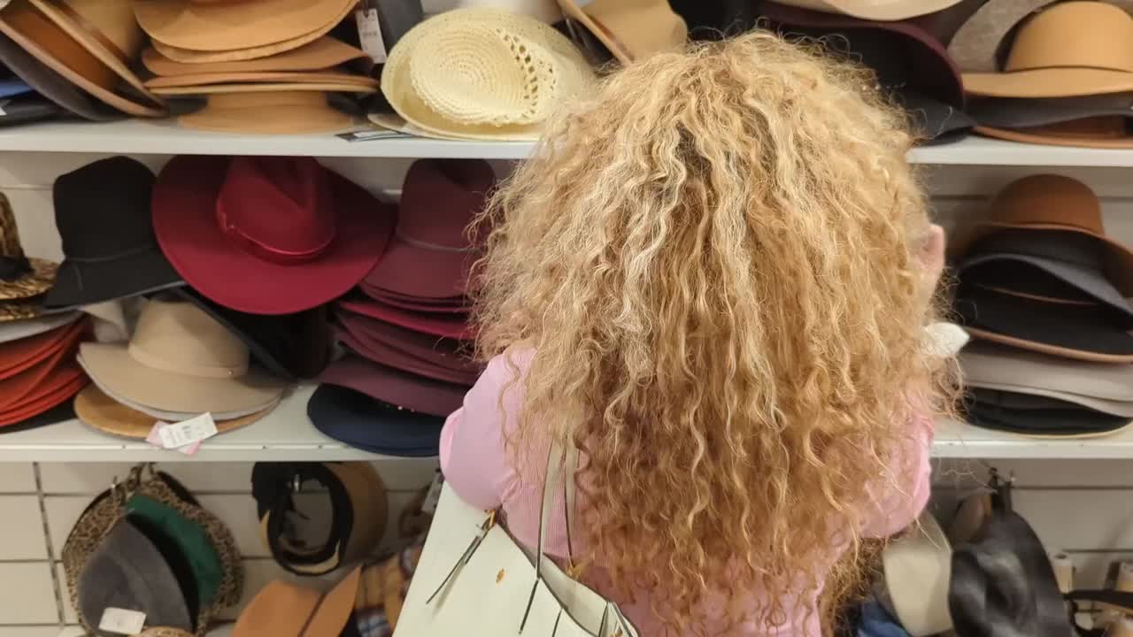 una mujer latina asombrosamente hermosa con el pelo largo va a comprar sombreros en una pila de sombreros que están a la venta en una tienda de ropa