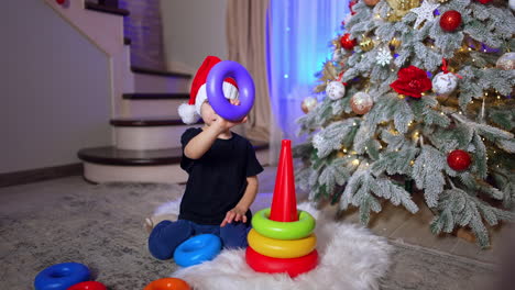 two year old toddler in santa cap plays with pyramid. lovely child having fun at home at christmas.