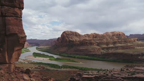 Eine-4K-Drohnenaufnahme-Von-Steilen-Klippen-Und-Einer-Eisenbahnstrecke,-Die-Entlang-Des-Colorado-River-Verläuft-Und-Durch-Die-Einzigartige-Und-Raue-Wüstenlandschaft-In-Der-Nähe-Von-Moab,-Utah,-Schneidet