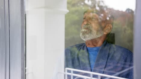 Glücklicher-älterer-Gemischtrassiger-Mann,-Der-Unverändert-In-Zeitlupe-Durch-Das-Fenster-Schaut