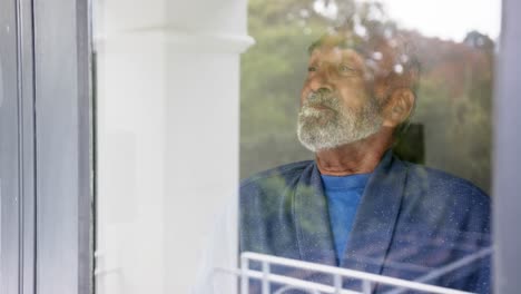 happy senior biracial man looking through window, unaltered, in slow motion