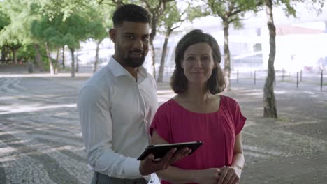 Two-cheerful-workers-posing-with-tablet-outdoor.