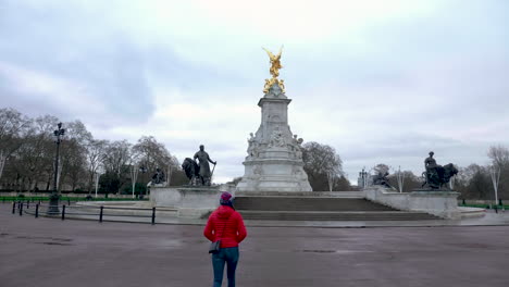 scatto statico di giovane donna con giacca rossa che cammina in una piazza vuota di buckingham palace, senza turisti