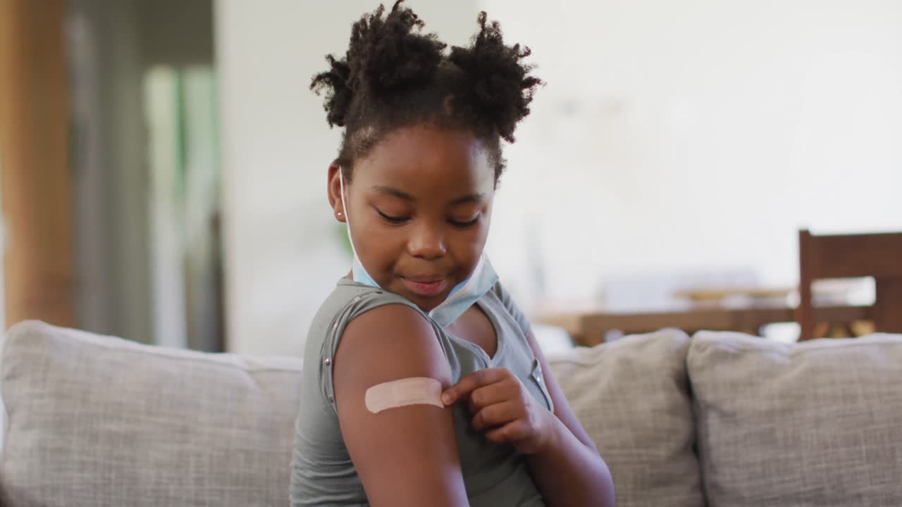 Jeune fille afro-américaine portant un masque facial et montrant un bandage sur son bras