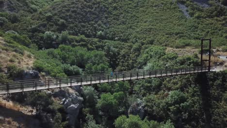 Drone-Shot-following-an-active-man-running-on-an-outdoor-hanging-suspension-bridge-above-Bear-Canyon-in-Draper-City,-Utah