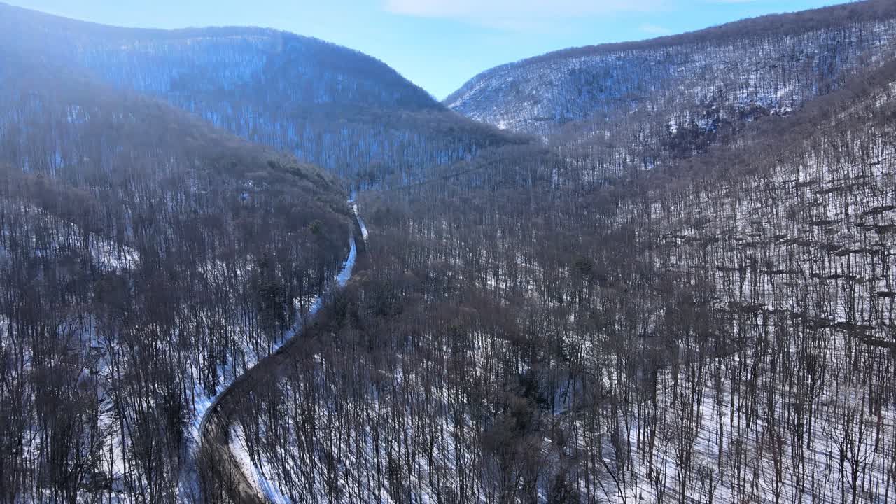 Riprese aeree con drone di una valle di montagna innevata e una strada all'inizio della primavera, in una giornata di sole, nella catena montuosa degli Appalachi, subito dopo la fine dell'inverno, con foreste, neve, sole e cieli azzurri