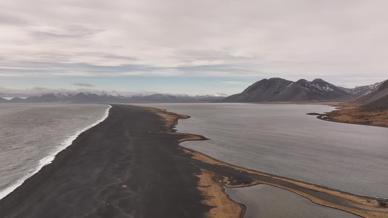 Aerial view of Vestrahorn mountain and the dramatic black sand beach at Stokksnes Peninsula, Iceland. Coastal beauty meets volcanic terrain under cloudy skies.