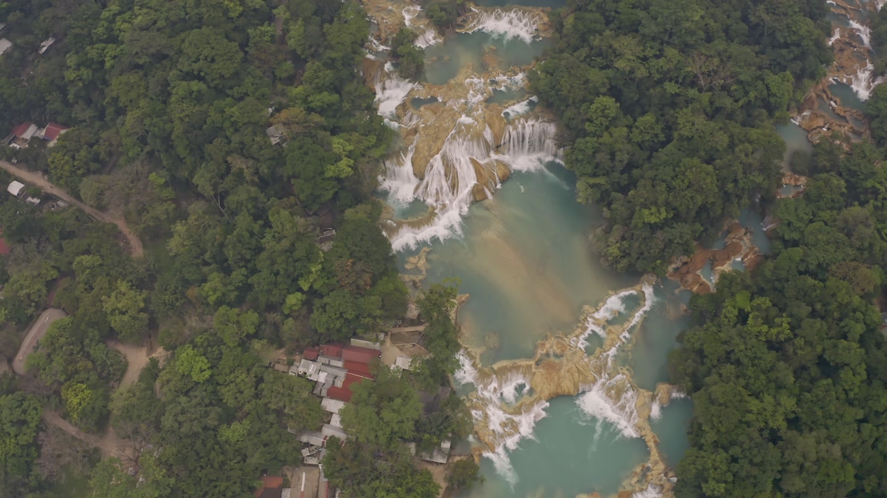 Aerial drone shot of the Agua Azul waterfalls in Chiapas, Mexico. The perspective shows the stunning turquoise water cascading over limestone formations.