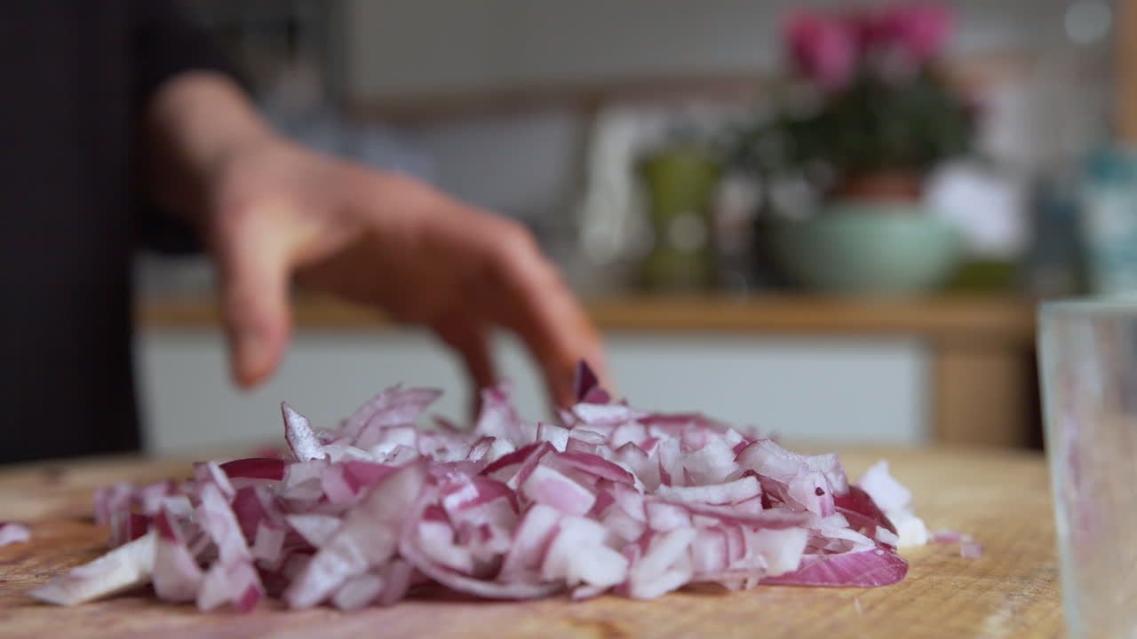 Close up pan woman's hand chopping Italian red onions with a rounded sharp knife on a wooden board in her kitchen, then slowly filling glass lunch box