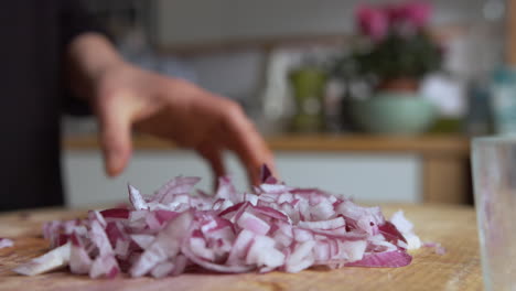 Close-up-pan-woman's-hand-chopping-Italian-red-onions-with-a-rounded-sharp-knife-on-a-wooden-board-in-her-kitchen,-then-slowly-filling-glass-lunch-box