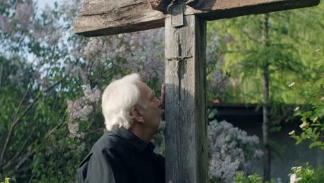 elderly man in a garden, paying homage to a wooden cross