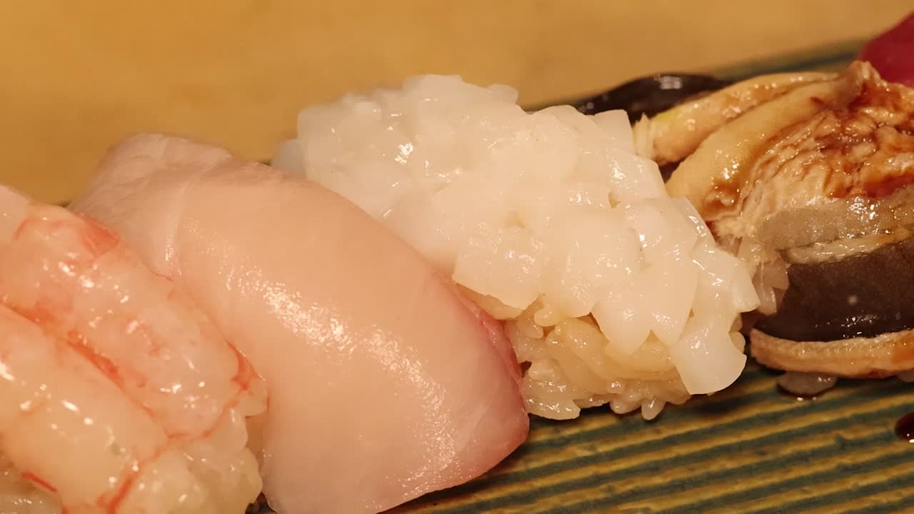 Macro view of a chef's hand seasoning a row of fresh assorted nigiri sushi