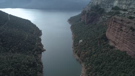 Morro-de-l'Abella-reservoir-aerial-establishing-view-over-curving-river-tilt-up-to-stunning-mountain-ridge-Catalonia,-Spain