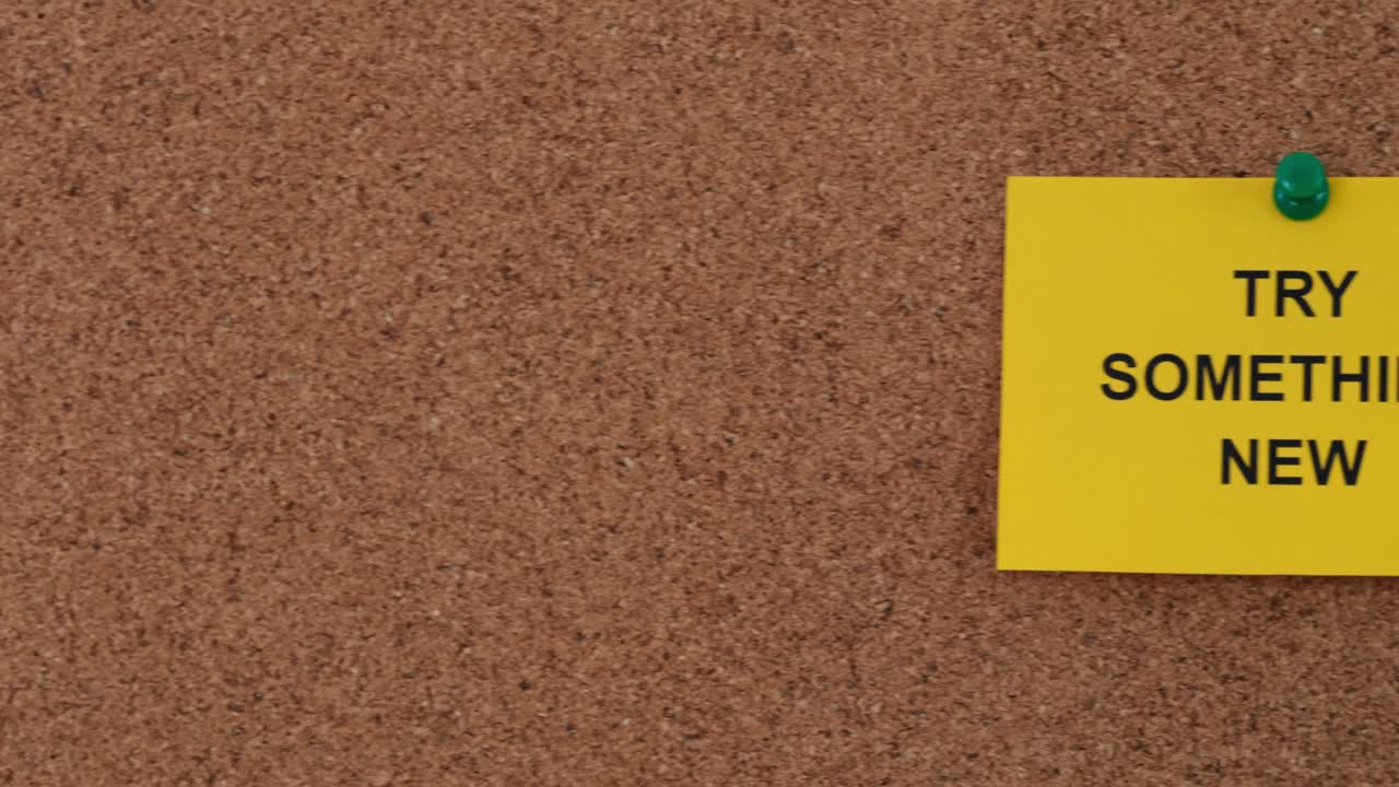 A sticky note with the words Try Something New on it pinned to a cork board.
