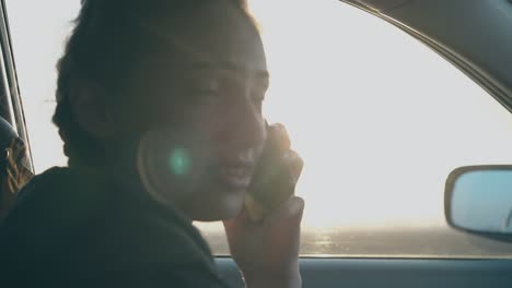 woman sits in car holds black smartphone and talks