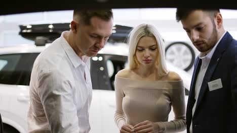 car agent showing trunk from inside to customers in automotive dealership showroom