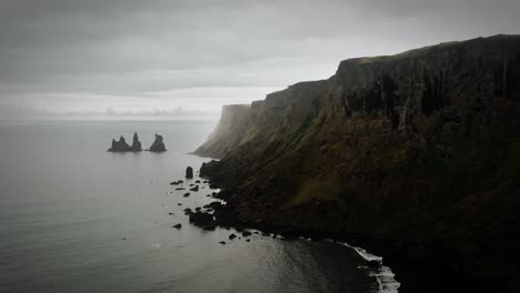 cinematic cliff aerial black sand beach rock formation, ocean scenery, moody dark scenery, town vik, reynisdrangar iceland