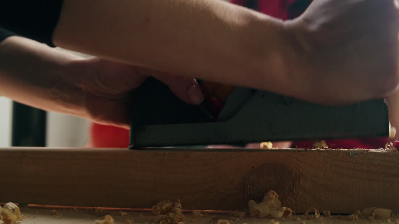 Close-up of Hands Planing Wood with a Hand Plane in a Workshop