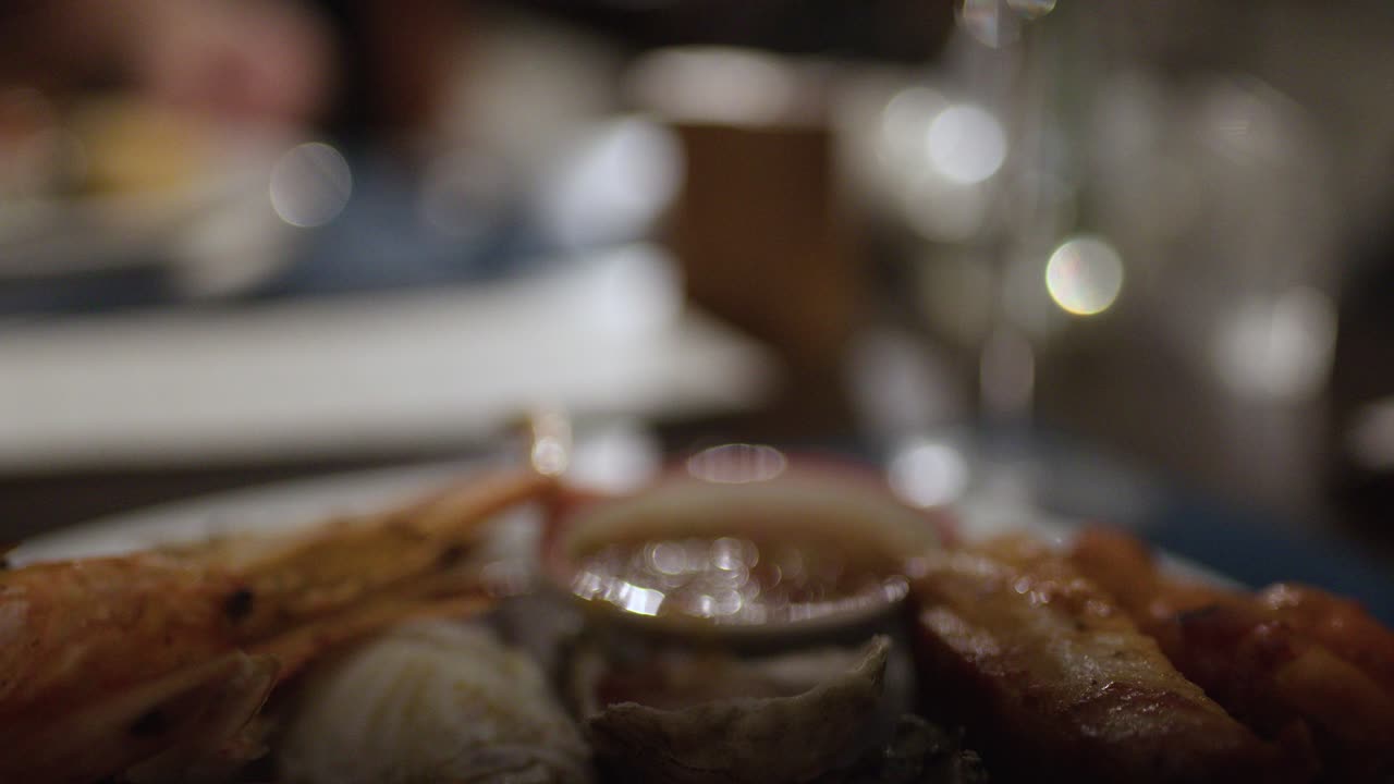 Plate of shrimp, oyster, and crab with sauce in dimly lit Bangkok restaurant, static close-up