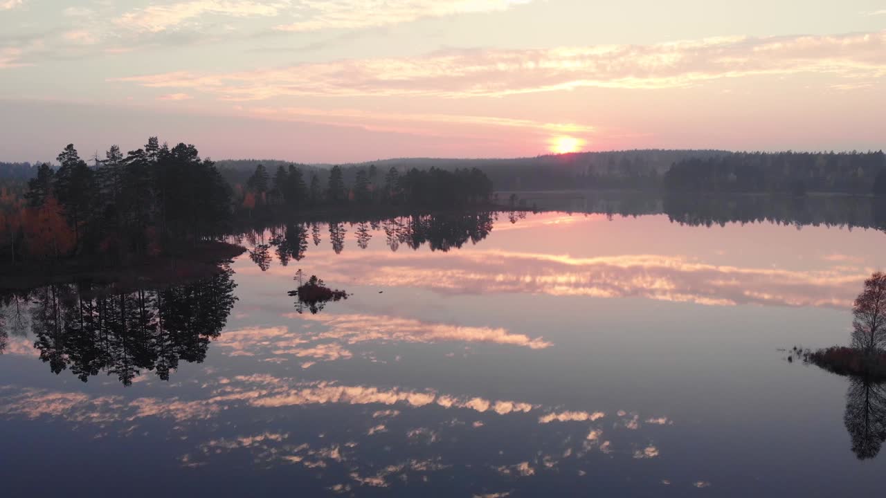 Flygvy över en perfekt speglad sjö vid solnedgången i en skog under hösten.