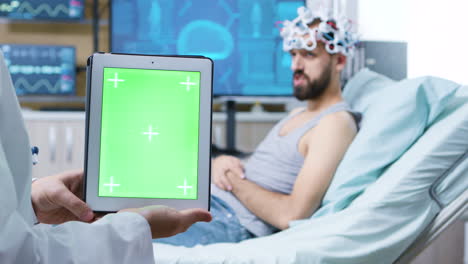 médico en una clínica de neurología sosteniendo una tableta con pantalla verde