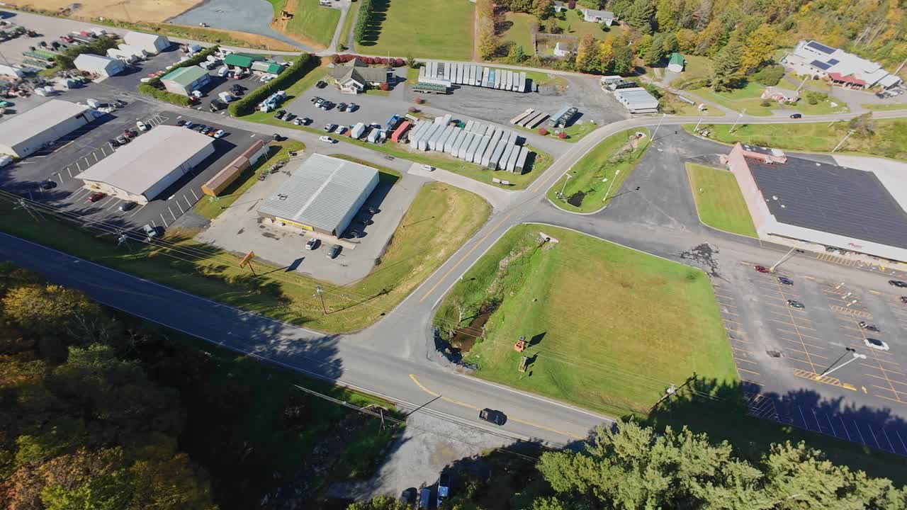 Luftfoto af Tennessee Industripark, USA, der viser lagerbygninger, parkeringspladser, lastbiltrailere, vejkryds, omkringliggende træer med efterårsløv og skarpt sollys. Droneopmåling
