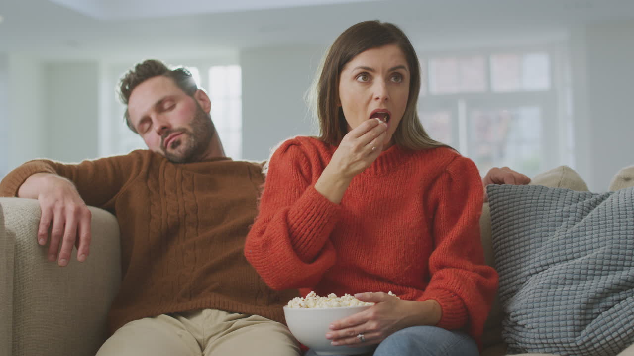 el hombre se queda dormido mientras la pareja se sienta en el sofá con palomitas de maíz viendo la televisión.