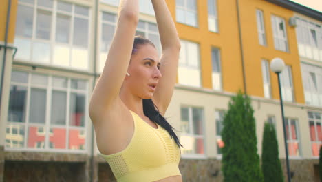 una mujer joven en el parque con auriculares hace yoga. haciendo yoga en la hierba contra el fondo de las casas en el parque de la ciudad en cámara lenta