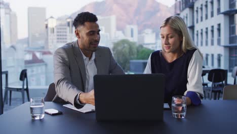 video of two diverse male and female colleagues discussing and using laptop in office