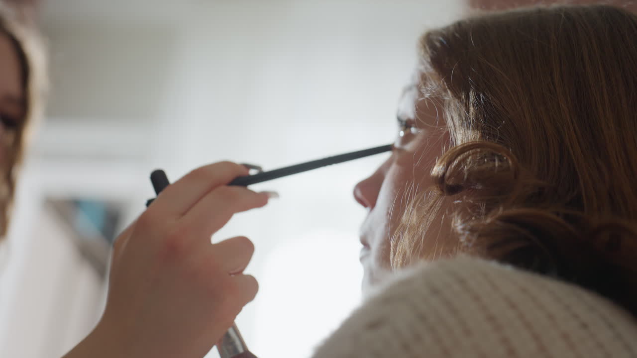 Profile View Of Woman With Makeup Artist, Calm Studio Setting With Focused Cosmetic Application, Natural Lighting Captures Woman As Artist Delicately Applies Mascara With Careful Hand