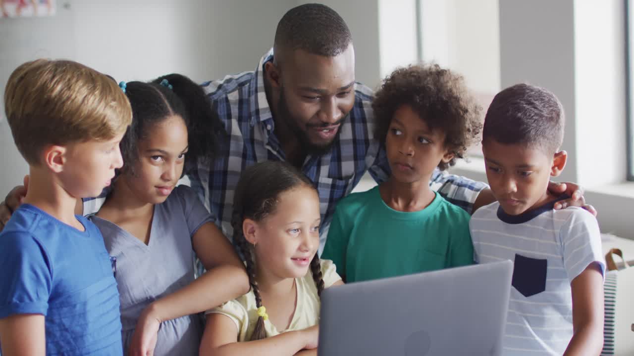 Video of happy african american male teacher and class of diverse pupils working on laptop