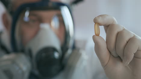 un científico médico en una compañía farmacéutica desarrollando un medicamento en un laboratorio en una pantalla de respirador de vidrio sostiene un nuevo medicamento una píldora amarilla un antibiótico contra el virus y lo mira.