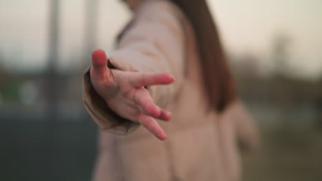 en una escena llena de enfoque suave, una persona con una chaqueta de melocotón extiende su mano alegremente hacia la cámara, creando un momento de interacción dinámica con el entorno.