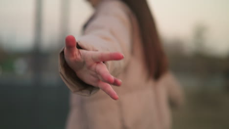 in a scene filled with soft focus, a person in a peach jacket spreads their hand joyfully towards the camera, creating a moment of dynamic interaction with the environment. the background is blur