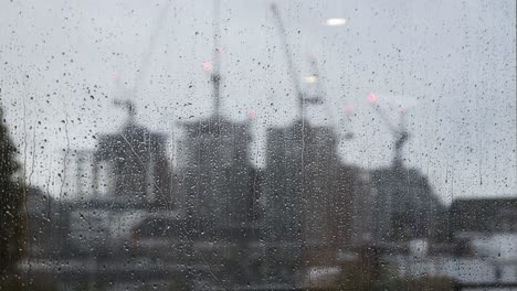 Lluvia-Cayendo-Sobre-La-Ventana-Con-Grúas-De-Construcción-Borrosas-En-El-Fondo