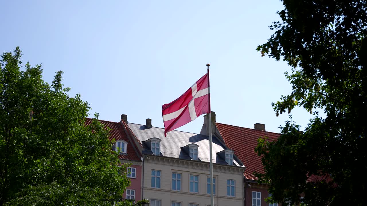 bandera danesa ondeando en el aire con edificios europeos tradicionales en el fondo, copenhague