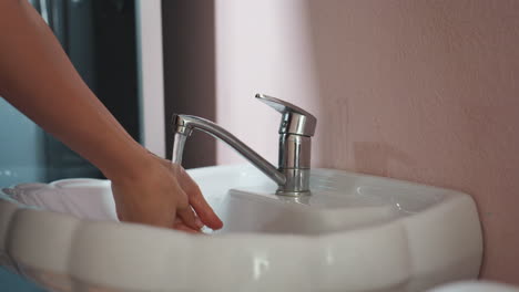 light skin woman washing hands in white sink with silver faucet, letting water flow while gently cleaning palms and fingers, preparing to dry hands using clean white towel in cozy bathroom setting