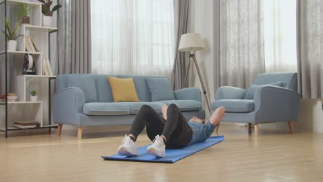 hombre atlético asiático en forma con ropa deportiva haciendo ejercicios abdominales en casa en su espaciosa y luminosa sala de estar
