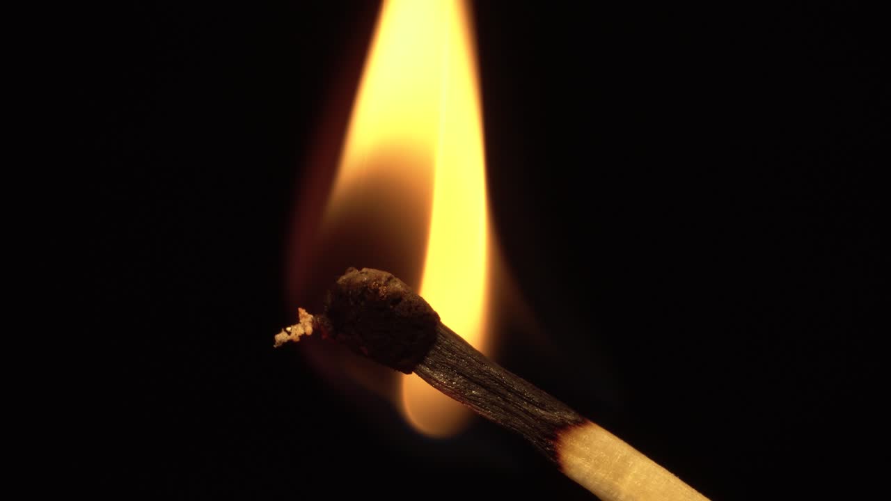 Closeup matchstick head catching fire and igniting and burning, macro, black background