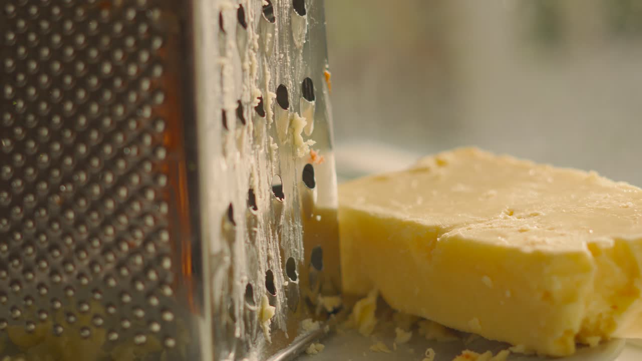 Descending Camera View of Grater After Grating Cheddar with Block of Rustic Cheese Resting on Plate in Natural Light. Dairy Based Food Product