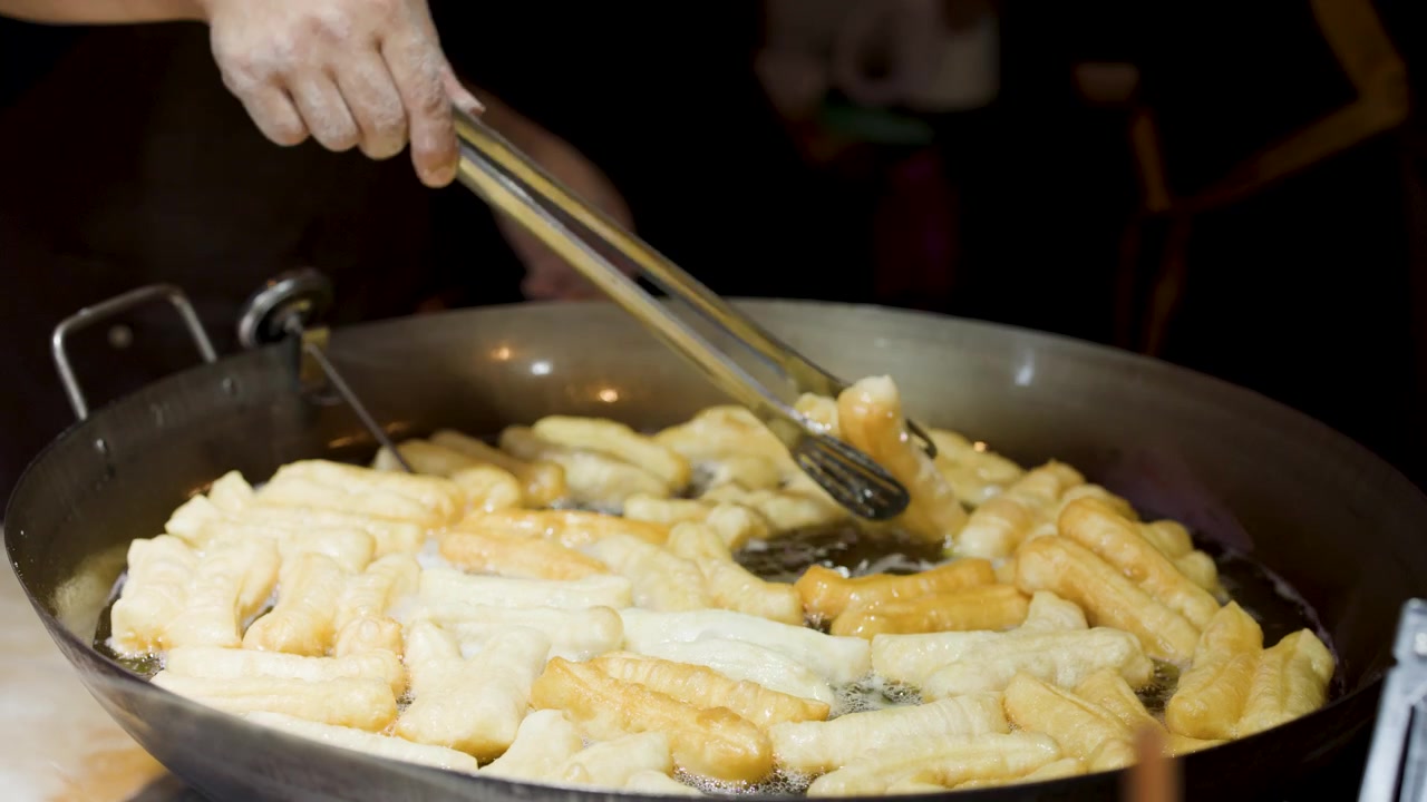 Chef che frigge bastoncini di pasta Youtiao in un grande wok