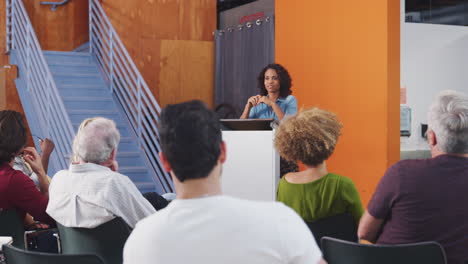 mujer en el podio presidiendo una reunión de vecindario en un centro comunitario